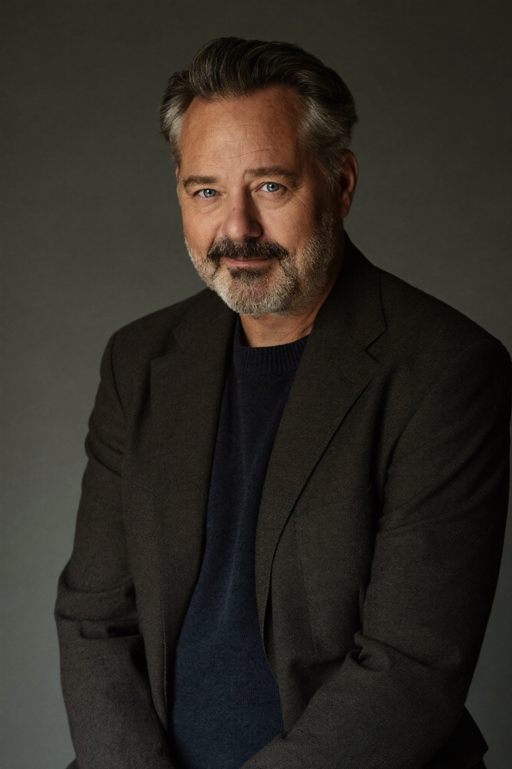 A man with a greying beard, in a charcoal blazer over a navy sweater